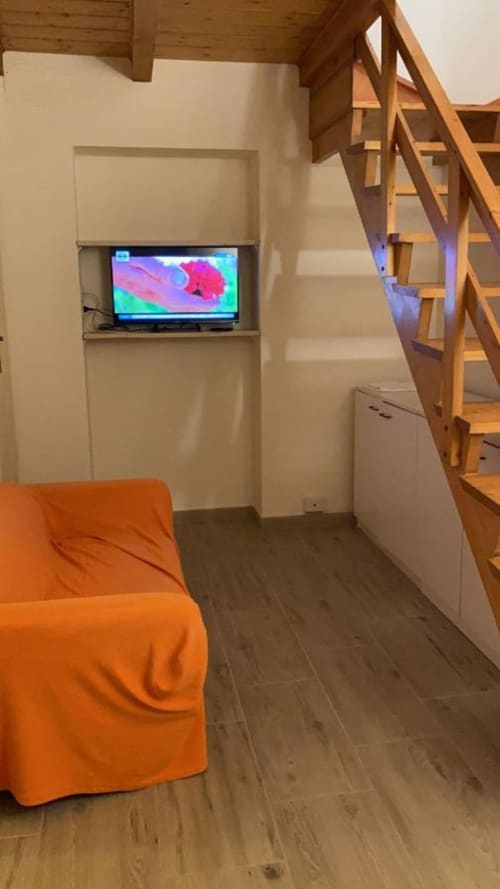 Camera con soppalco moderno a My Florentine Apartment: TV, scala in legno, sedia arancione e pavimento in legno scuro