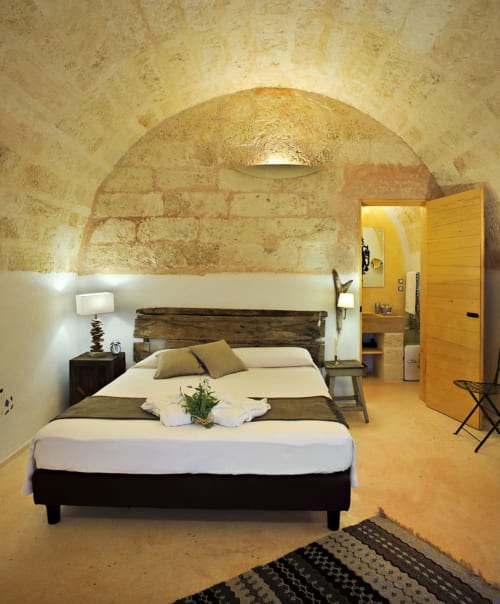 Camera Pesce presso Masseria Picca Picca con soffitto in pietra ad arco, letto in legno, biancheria bianca e pavimento in cotto a Morciano di