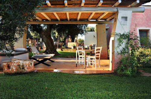 Patio con pergolato in legno presso Masseria Picca Picca: tavolo da pranzo, lettini, albero maturo e prato curato a Morciano