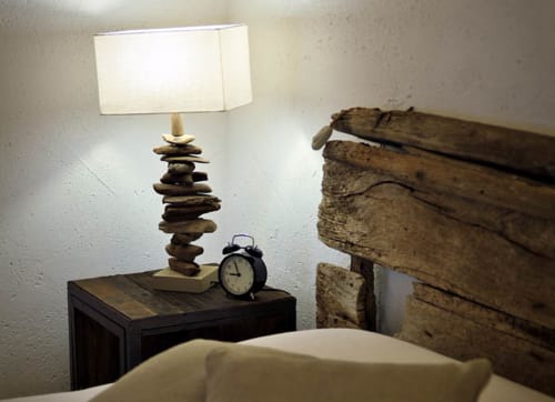 Comodino nella camera Pesce di Masseria Picca Picca con lampada in pietra, sveglia e testata rustica in legno