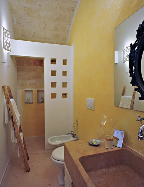 Bagno luminoso e giallo presso Masseria Picca Picca con lavabo in terracotta, water bianco, specchio e doccia a Morciano di