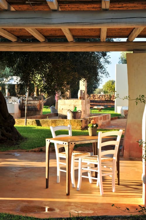 Veranda coperta con tavolo in legno e sedie bianche con vista sul giardino di Masseria Picca Picca, Morciano di Leuca