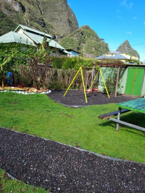 Jardin de la villa Au pied des Sources à Cilaos avec balançoire jaune, pelouse verte et spectaculaire décor de falaises rocheuses