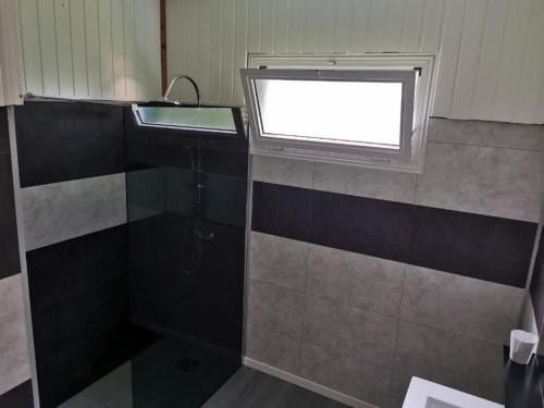Salle de bain moderne au carrelage noir et gris à la villa Au pied des Sources à Cilaos, avec douche à l'italienne et fenêtre