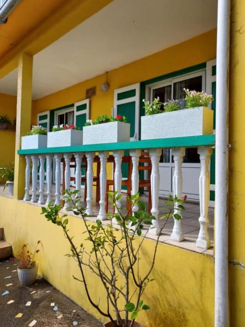 Balcon coloré d'une villa à Au pied des Sources, Cilaos avec rampes blanches, fleurs en pots et volets verts