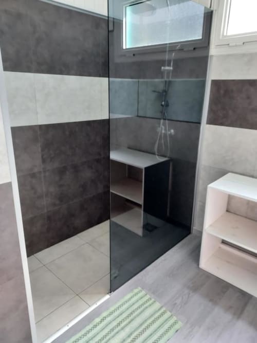Salle de bain moderne avec douche à l'italienne, tapis rayé et carrelage gris à l'hôtel Au pied des Sources à Cilaos