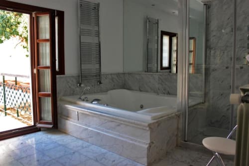 Lujoso baño de la Suite Comares Granada con bañera de mármol, ducha tipo lluvia, toallero climatizado y acceso a balcón