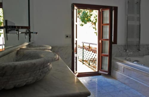 Baño de lujo en Suite Comares Granada con bañera de piedra, puertas de terraza abierta y vistas panorámicas de la ciudad