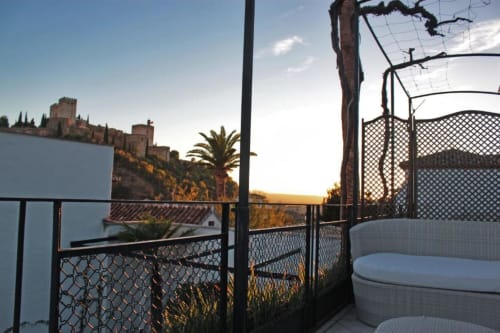 Terraza Suite Comares en Granada con vistas al palacio de la Alhambra al atardecer, zona de descanso frente a la fortaleza histórica.