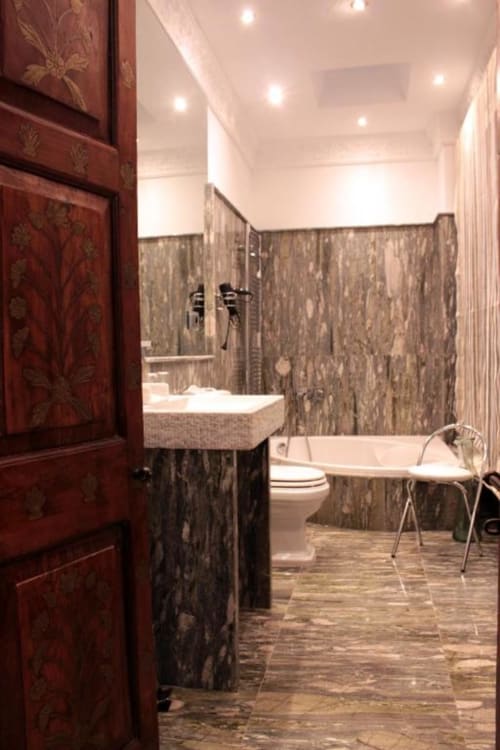 Baño moderno del hotel Suite Comares en Granada con paredes de baldosas de piedra, lavamanos de cerámica, inodoro y bañera con grifería cromada