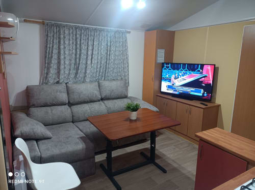 Modern living room with gray sofa, flat screen TV, and wooden table in Bungalow B at Buda Beach hotel, Chipiona
