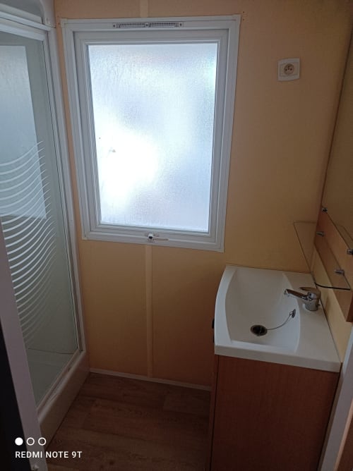 Bathroom in Bungalow B at Buda Beach Chipiona with shower, sink, and frosted window overlooking garden