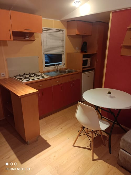 Modern kitchen and dining area in Bungalow C at Buda Beach hotel, Chipiona with red cabinets, gas stove, and round white