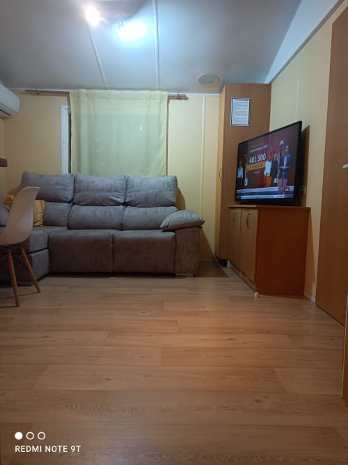 Modern living room in Bungalow D at Buda Beach hotel, Chipiona, with gray sofa, flat-screen TV, and wooden flooring