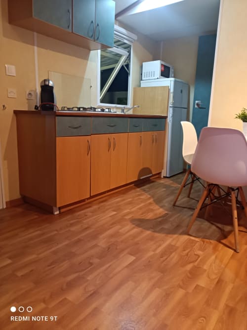 Modern kitchen area in Bungalow E at Buda Beach Chipiona with orange cabinets, stainless steel appliances, and dining chairs