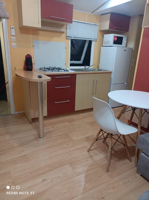 Modern kitchen and dining area in Bungalow F at Buda Beach hotel, Chipiona with red cabinets, gas stove, and white dining