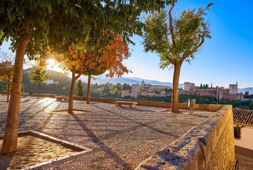 Vista del palacio de la Alhambra desde la terraza de la Suite Comares en Granada con árboles otoñales y montañas al atardecer