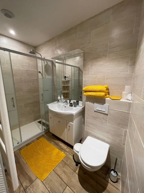 Salle de bain moderne à La Montagnette B&B à Moutiers avec douche à l'italienne, vasque blanche et serviettes et tapis jaunes