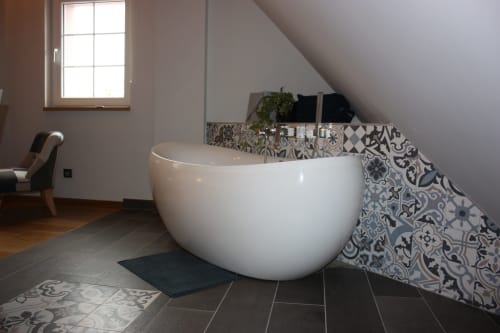 Baignoire blanche moderne dans la salle de bains mansardée du gîte Théière & Couverts à Cernay, entourée de carreaux décorés