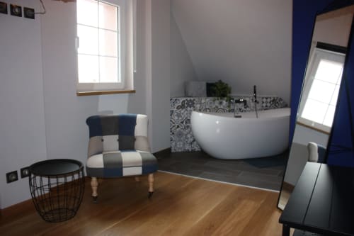 Suite de salle de bain moderne à Théière & Couverts : baignoire îlot courbe, carrelage à motifs, fauteuil et parquet.