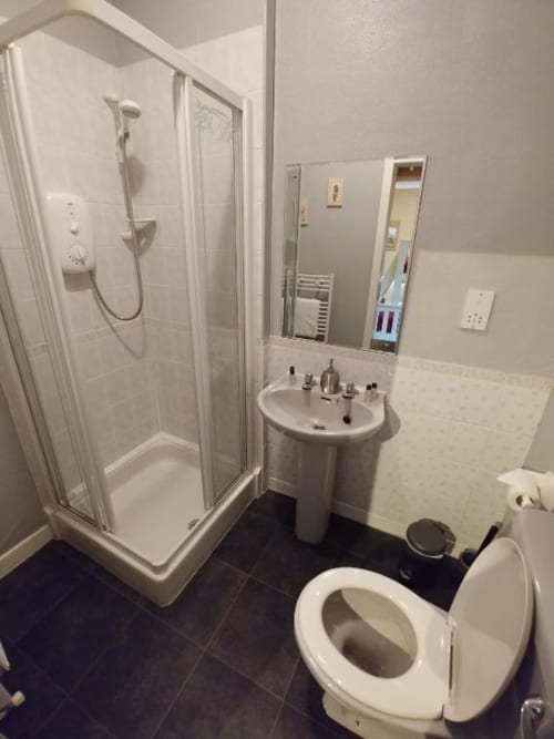 Modern bathroom at Arrochoile Glasgow B&B with shower enclosure, pedestal sink, toilet, and dark tile flooring