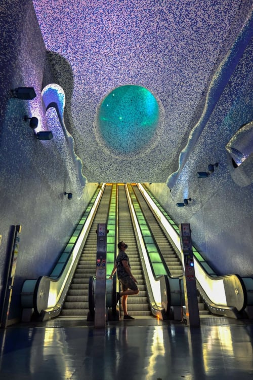 Persona su scala mobile illuminata sotto la cupola turchese dell'hotel Encanto, Napoli