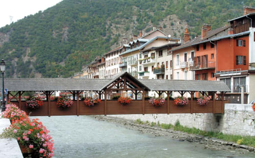 Pont en bois fleuri surplombant la rivière, bâtiments alpins colorés et montagnes boisées à Moutiers