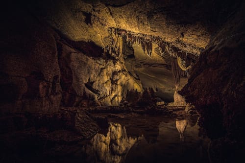 Grotta sotterranea con stalattiti, riflessi d'acqua e illuminazione dorata calda a Encanto Naples