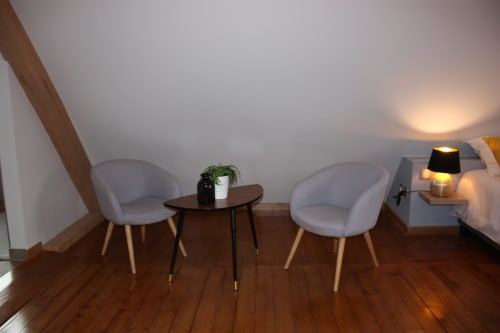Chambre douillette sous les toits à Théière & Couverts avec deux fauteuils gris, petite table et éclairage chaleureux