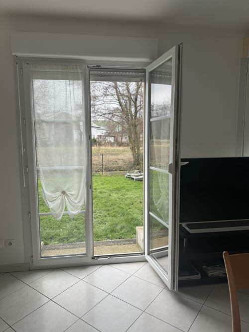 Open glass doors revealing lush garden at Le Clos De La Vallée cottage in Bellengreville, with green lawn and bare trees