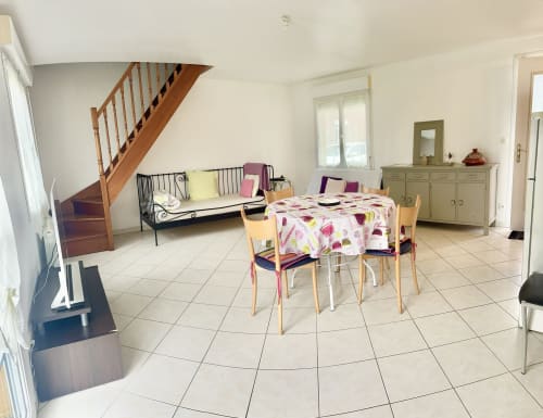 Le Clos 2 cottage dining area with wooden staircase, pink tablecloth, seating for four, and garden view in Bellengreville