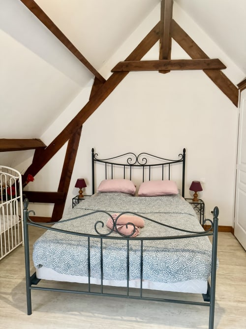 Cozy bedroom in Le Clos cottage with exposed wooden beams, wrought iron beds, pink pillows, and cream walls