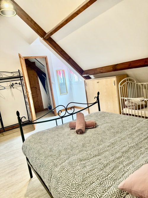 Spacious bedroom in Le Clos De La Vallée cottage with wrought iron bed, beamed ceiling, and garden view in Bellengreville,