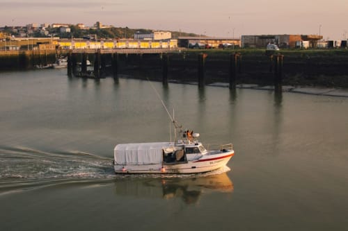 Bateau de pêche dans le port de Boulogne-sur-Mer avec bâtiments industriels jaunes et pieux de quai visibles