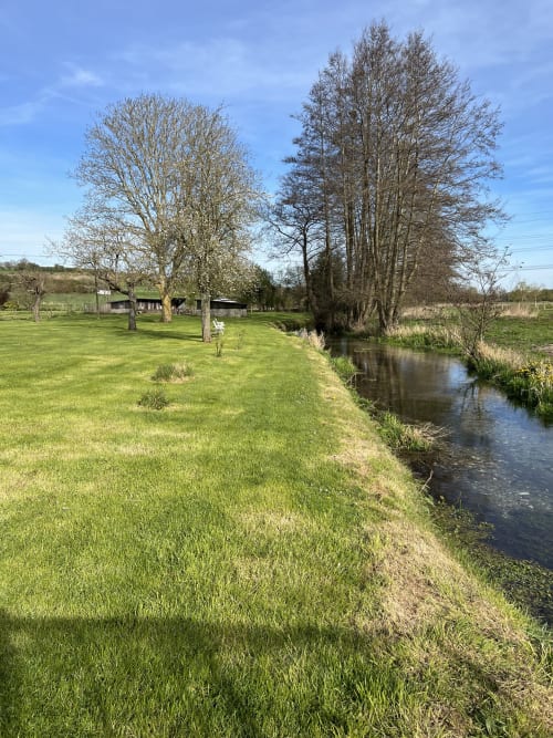Lush green garden with stream at Le Clos De La Vallée cottage in Bellengreville, France