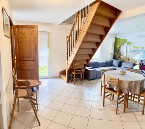 Open-plan living area in Le Clos cottage with wooden staircase, dining table, blue sofa, and kitchen in Bellengreville,