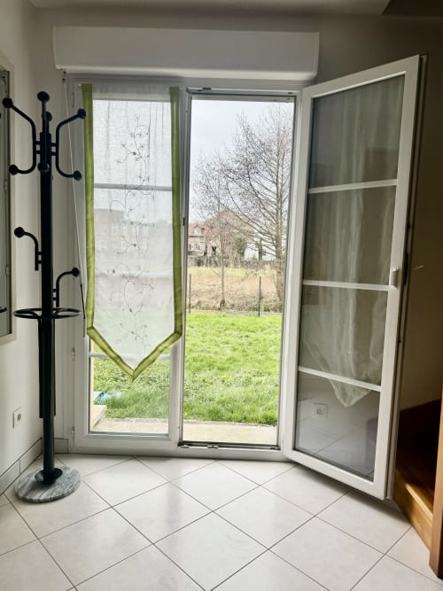 Open glass patio doors revealing lush garden view at Le Clos cottage, with seating area and nature outside