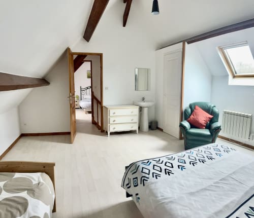 Bright attic bedroom at Le Clos De La Vallée cottage with bed, green armchair, white dresser, and skylights
