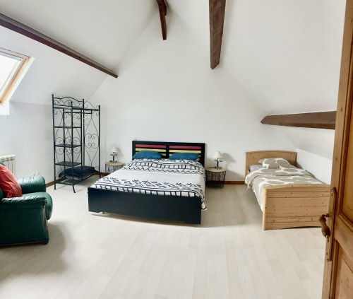 Spacious bedroom in Le Clos cottage with two beds, exposed beams, white walls, and green armchair at Le Clos De La Vallée,