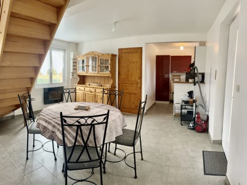 Dining area in Le Clos 4 cottage with round table, kitchen access, wooden furniture, and garden view in Bellengreville