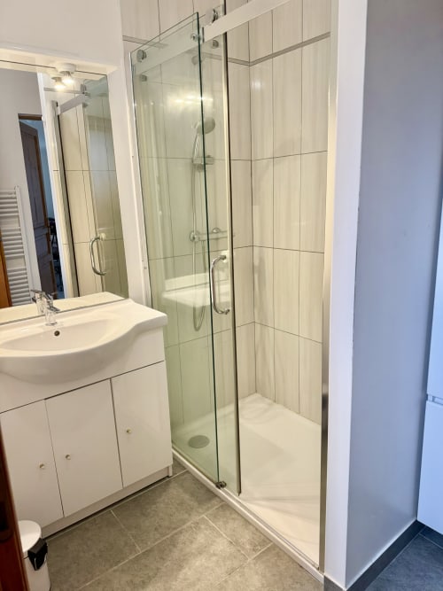 Modern bathroom with glass shower enclosure, white sink vanity, and cream tile walls at Le Clos cottage
