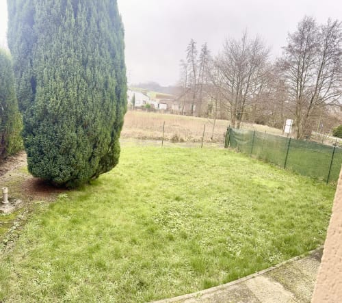 Lush green garden with manicured lawn, tall evergreen hedges, and countryside views at Le Clos De La Vallée cottage in