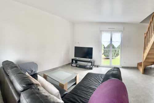 Modern living room in Le Clos 4 cottage with leather seating, flat-screen TV, wooden staircase, and garden view doors in
