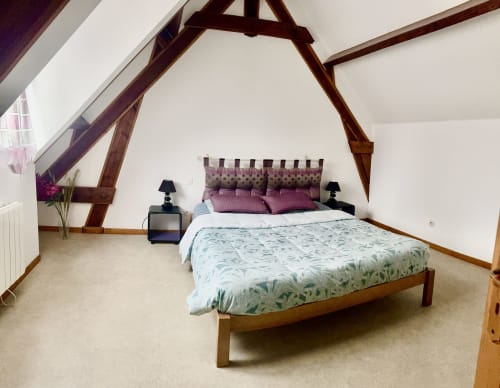 Spacious attic bedroom at Le Clos De La Vallée cottage with exposed wooden beams, wooden bed, purple accents, and garden