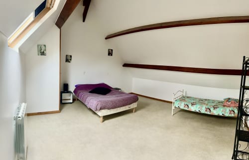 Cozy bedroom in Le Clos De La Vallée cottage with purple bedding, child's bed, exposed beams, and garden view in