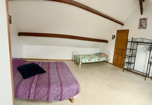 Spacious attic bedroom at Le Clos De La Vallée cottage with two beds, purple bedding, wooden beams, and garden views in