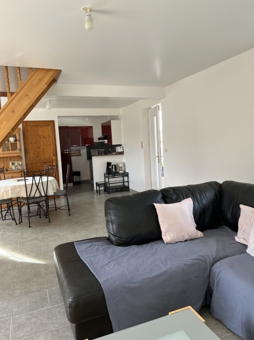 Black leather sofa with blue blanket in Le Clos 4 cottage living area, Bellengreville, with kitchen and wooden stairs visible