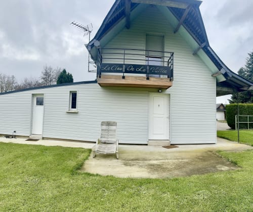 Le Clos De La Vallée cottage with white siding, curved blue roof, and balcony in Bellengreville garden setting