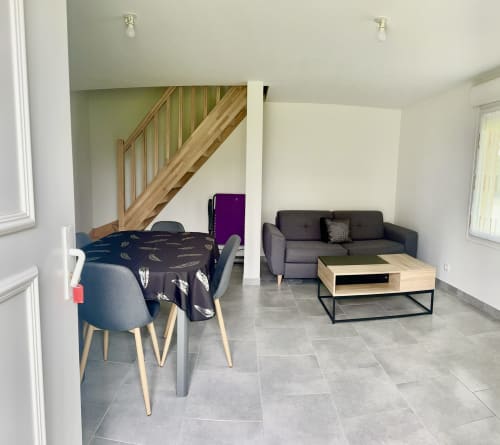 Le Clos 5 cottage interior with dining area, dark table, gray sofa, wooden staircase, and stone flooring at Le Clos De La