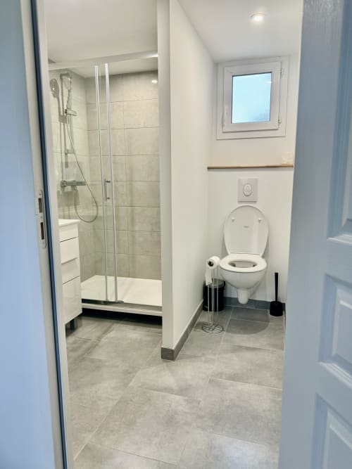 Modern bathroom at Le Clos De La Vallée cottage with shower enclosure, white toilet, gray tile flooring, and window in